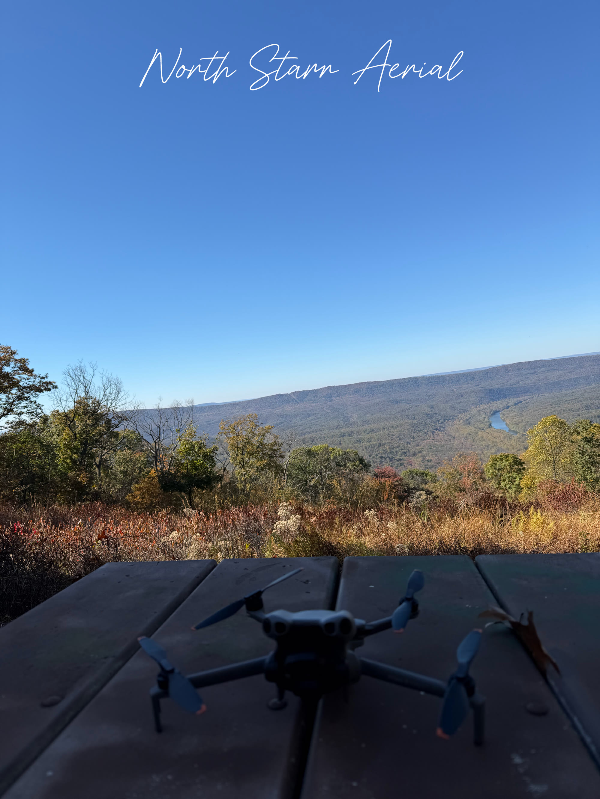 Compact drone on a picnic table overlooking a fall river valley, with North Starr Aerial script at the top