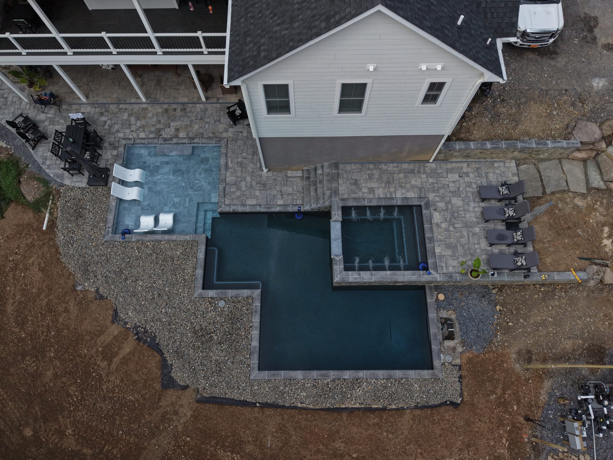 Top-down aerial view of a newly finished backyard pool with a raised spa, sun shelf loungers, and paver patio